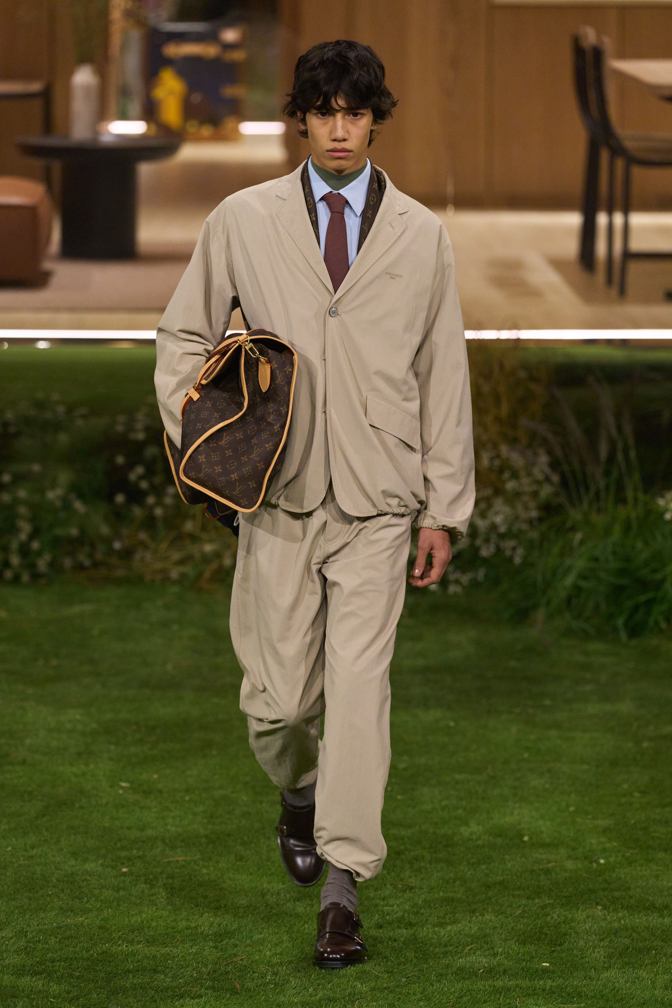 Louis Vuitton 26FW 男装以“当代绅士的旅行状态”为核心，在花园式场景中展开一场关于移动、身份与功能的叙事。功能夹克、细致西装、学院感针织与标志性包袋并行出现，色彩回归卡其、橄榄绿、灰褐与深红，呈现出低调却高度可穿的奢华现实主义。系列强化了“穿着中的生活感”，将品牌传统的旅行基因转译为更克制、更日常的现代衣橱方案-顽石频道趋势研究